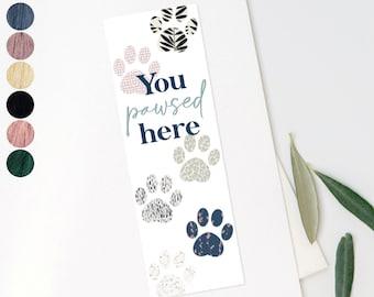 May include: A white bookmark with a blue paw print design and the text "You pawsed here".