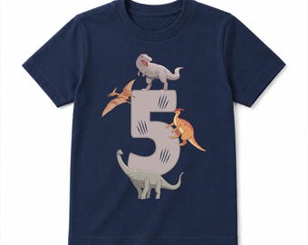 May include: A navy blue short-sleeve t-shirt featuring a large, light gray number five graphic in the center. The number is decorated with black claw marks and surrounded by four illustrated dinosaurs, including a T-Rex, a pterodactyl, a long-necked sauropod, and a bipedal dinosaur.