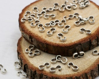 May include: Small, silver-colored jewelry connectors scattered on two wooden slices. The connectors have a figure-eight shape, and the wood slices have a natural, rustic appearance. The connectors are likely for jewelry making or crafting.