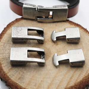 May include: Four silver-toned metal clasps for leather bracelets. Two clasps are rectangular with a small opening in the center. Two clasps are T-shaped with a small opening on the side.