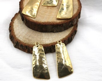 May include: Four gold-toned metal pendant charms with a hammered texture. The charms are rectangular with rounded corners and have a hole at the top for hanging.