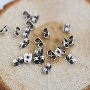 May include: A close-up of a group of silver earring backs on a wooden surface. The earring backs are designed to secure earrings to the earlobe.