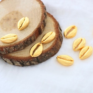 Peut inclure: Coquillages de cauris de couleur dorée sur une surface en bois. Les coquillages sont disposés en demi-cercle.
