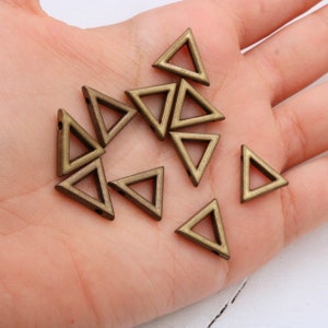 May include: A collection of antique gold triangle shaped metal beads. The beads have a hole at each point of the triangle.