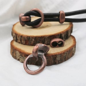 Peut inclure: Un ensemble de fermoirs en métal ton cuivre pour sangles en cuir. Les fermoirs sont en forme d'anneau avec un crochet d'un côté. Les fermoirs sont sur une surface en bois.