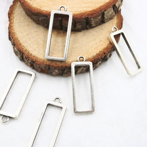 Peut inclure: Cinq cadres de pendentif en métal argenté de forme rectangulaire. Les cadres sont ouverts et prêts à être remplis de résine, de verre ou d'autres matériaux.