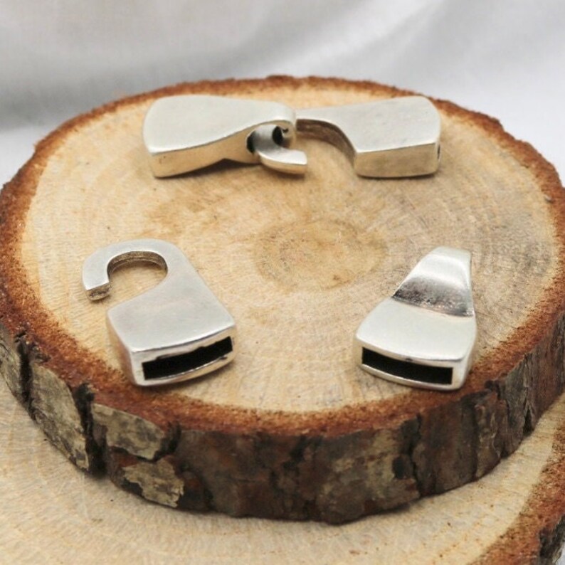 May include: Four silver metal clasps for jewelry making. The clasps are rectangular with a rounded edge and a small opening on one side.