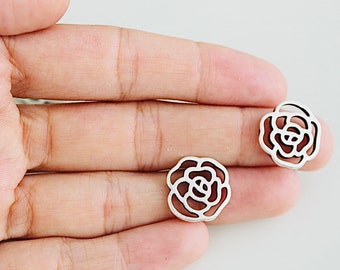 May include: A pair of silver earrings with a delicate rose design. The earrings are shown on a hand, with the rose design facing the viewer.