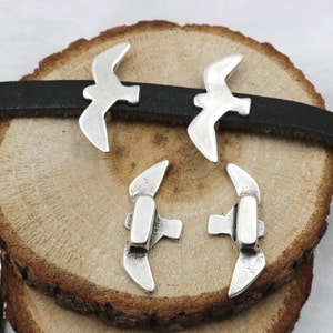 May include: Four silver bird charms, two with wings spread and two with wings folded, on a wooden surface.