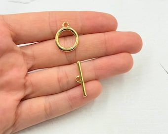 May include: Gold-toned metal toggle clasp with a round ring and a straight bar. The clasp is designed for jewelry making or crafting.