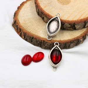 May include: Two silver-toned pendant settings with a teardrop shape and a small loop at the top. Two red glass cabochons are shown separately.