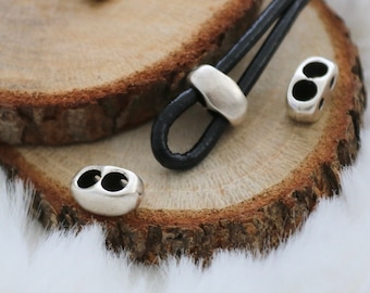May include: Silver metal cord ends with two holes, shown on a wooden surface with a black leather cord.