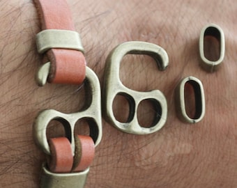 May include: A brown leather bracelet with a metal clasp. The clasp has a unique design with multiple holes. There are two extra metal pieces for the bracelet.