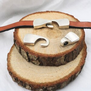 May include: Three silver metal clasps for leather straps. The clasps are on a wooden surface.