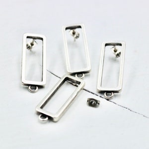 May include: Four silver rectangle shaped earring blanks with a post and loop on the back. The earring blanks are on a white surface.