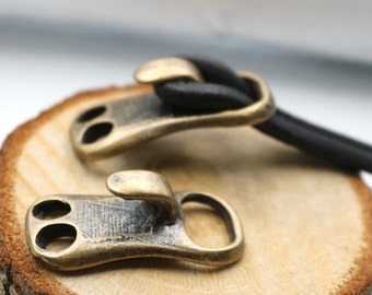 May include: Two antique brass clasps with a hook on one side and two holes on the other. The clasps are on a wooden surface.