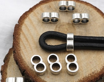 May include: Silver metal double loop cord ends for leather cord bracelets. The cord ends are shown on a wooden surface with a black leather cord threaded through one of the ends.