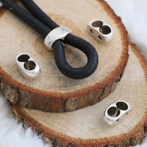 May include: A black leather cord with three silver metal clasps. The cord is lying on a wooden surface.
