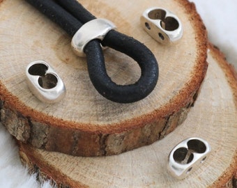 May include: A black leather cord with three silver metal clasps. The cord is lying on a wooden surface.