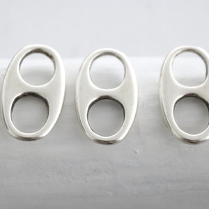 Könnte beinhalten: Drei silberne ovale Charms mit einem Doppel-Loop-Design.