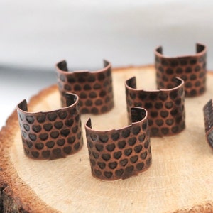 K&ouml;nnte beinhalten: Sechs kupferfarbene Metallringe mit einem Herzmuster. Die Ringe sind auf einer Holzoberfl&auml;che angeordnet.