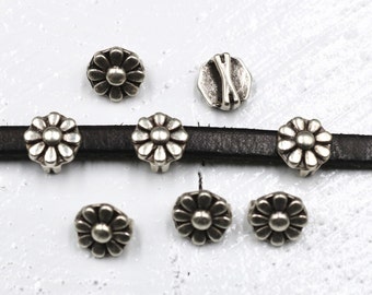 May include: Silver metal daisy flower charms with a silver metal buckle charm. The charms are on a black leather strap.