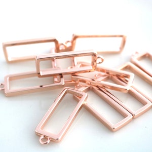May include: A group of rose gold metal rectangular frames with a small loop at the top. The frames are stacked on top of each other.