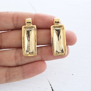 May include: Two gold-toned metal pendant trays with a rectangular shape. The trays are designed to hold a flat piece of glass or other material.