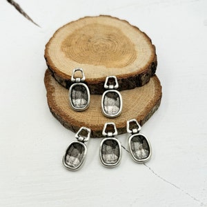 May include: Six silver-toned metal pendant charms with a rectangular shape and a loop at the top. The charms have a slightly textured surface.