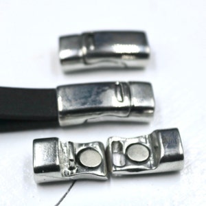 May include: Three silver-toned metal magnetic clasps for jewelry making. One clasp is attached to a dark brown leather cord, while the other two are shown separated to reveal the circular magnetic components and the locking mechanism.