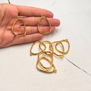 Puede incluir: Un conjunto de diez colgantes de metal de color dorado con forma ovalada irregular. Los colgantes tienen un acabado liso y brillante y un peque&ntilde;o bucle en la parte superior para sujetar una cadena o un cord&oacute;n.