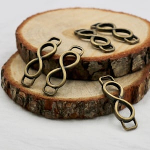 May include: Five antique gold-toned infinity symbol charms with a loop on each end. The charms are arranged on a wooden surface.