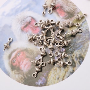 May include: A pile of silver-toned metal charms with a twisted design. The charms have a loop at the top for attaching to jewellery or other crafts.