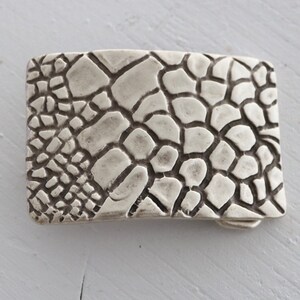 May include: A silver belt buckle with a textured, cracked pattern.