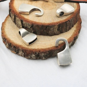 May include: Five silver metal hook and loop closures on a wooden surface. The closures are different shapes and sizes.
