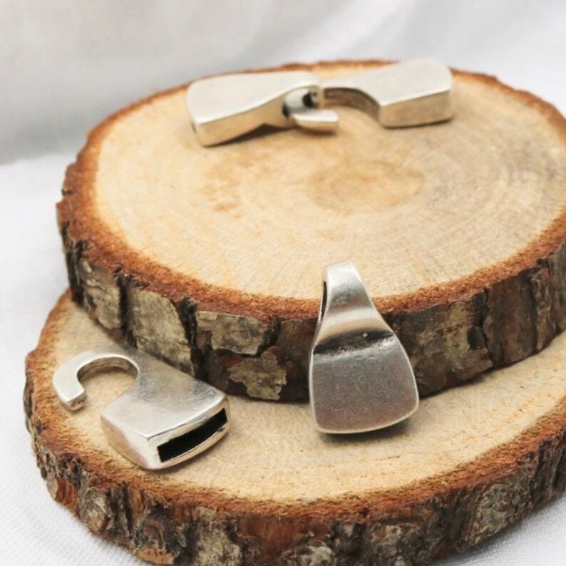 May include: Three silver metal clasps for jewelry making. The clasps are different shapes and sizes. The clasps are on a wooden surface.