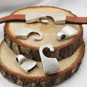 May include: Five silver-toned metal clasps with hook closures. The clasps are arranged on a wooden surface.
