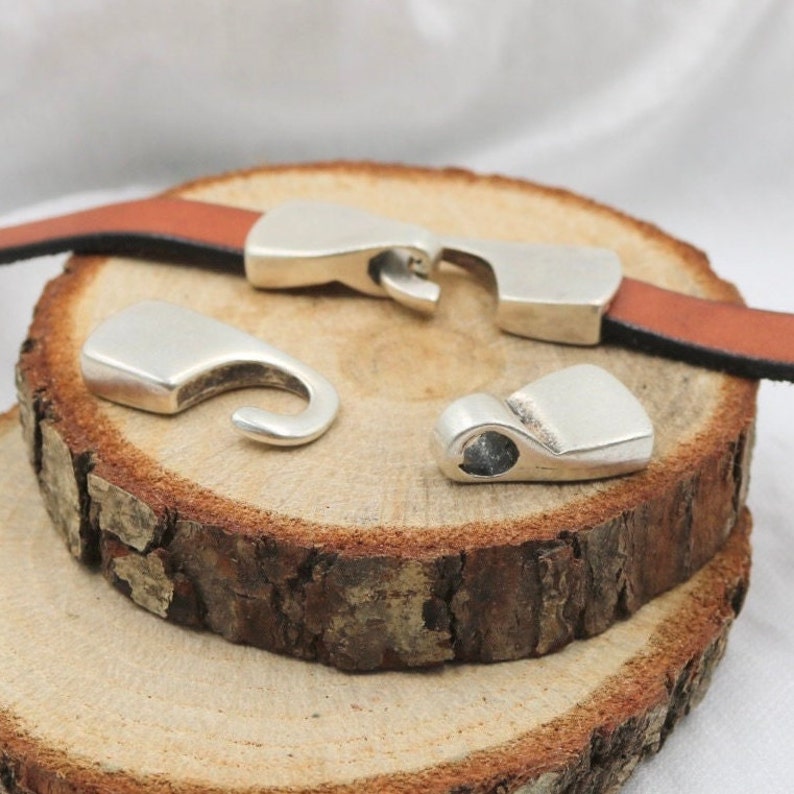May include: Three silver metal clasps for leather straps. The clasps are on a wooden surface.