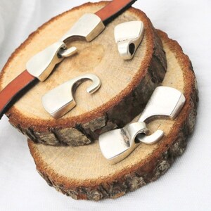 May include: Three silver metal clasps with a hook design. The clasps are on a wooden surface.