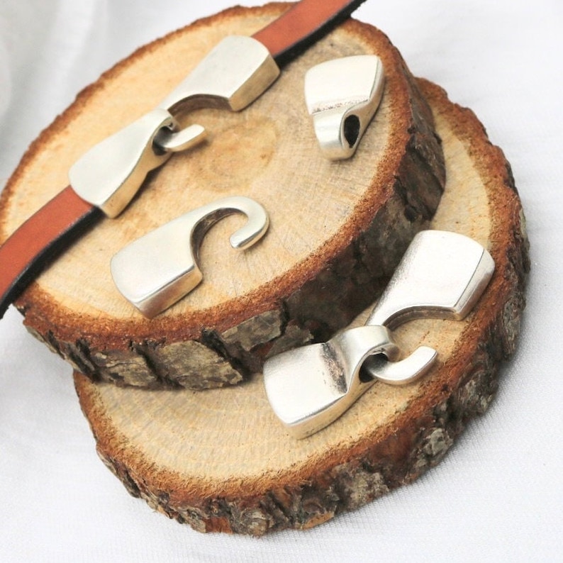 May include: Three silver metal clasps with a hook design. The clasps are on a wooden surface.