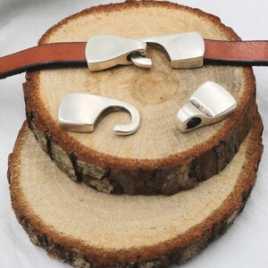 May include: Silver metal clasps for leather straps. The clasps have a hook and loop design.