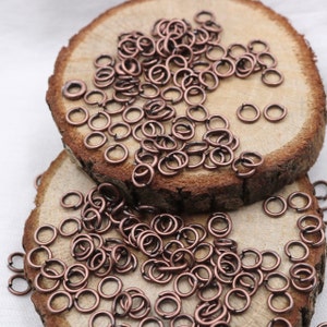May include: A pile of small, copper-colored jump rings on a wooden surface. The rings are about 5mm in diameter.
