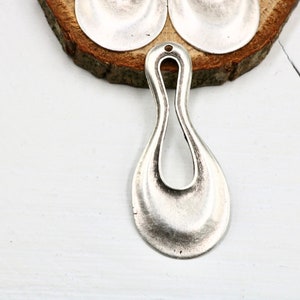 May include: Silver pendant with a teardrop shape and a cutout in the center. The pendant has a textured surface and a hole at the top for attaching a chain.