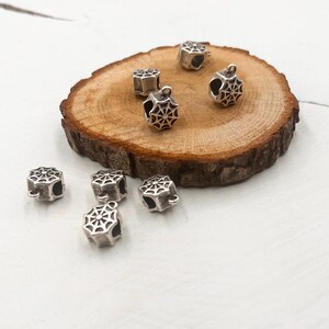 May include: Silver-toned metal charms with a spiderweb design. The charms have a loop at the top for attaching to jewelry or other crafts.