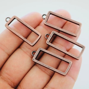 May include: Four copper-colored metal rectangular frames with a loop at the top for hanging. The frames are open and have a smooth, slightly textured finish.