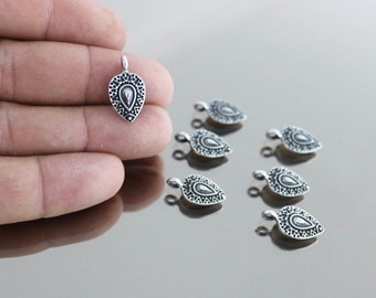 May include: Seven silver teardrop-shaped charms with an intricate design. The charms have a loop at the top for attaching to jewelry.