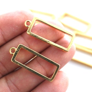 May include: Gold-toned metal rectangular frame pendant charms with a loop at the top. These charms are perfect for adding a touch of elegance to jewelry projects.
