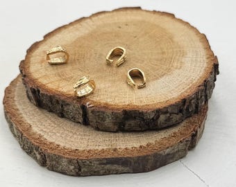 May include: Four gold-colored metal pendant bails on a wooden surface. The bails are small and have a U-shape.