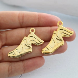 May include: Two gold-colored shoe charms with a winged design. The charms have a loop at the top for attaching to a bracelet or necklace.