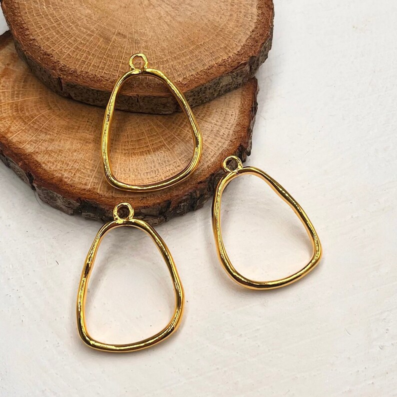 Puede incluir: Tres colgantes de metal de color dorado con forma redondeada irregular. Cada colgante tiene un peque&ntilde;o bucle en la parte superior para sujetar una cadena o una cuerda.